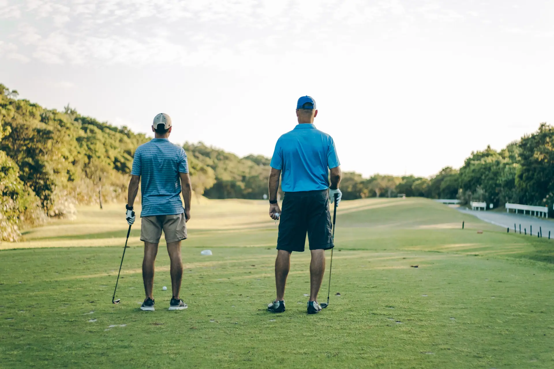 Two men stand facing the fairway on a golf course