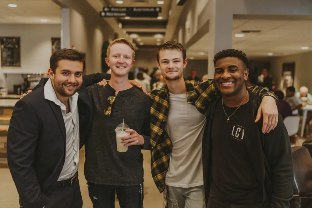 4 guys pose for a picture with arms across each others shoulders