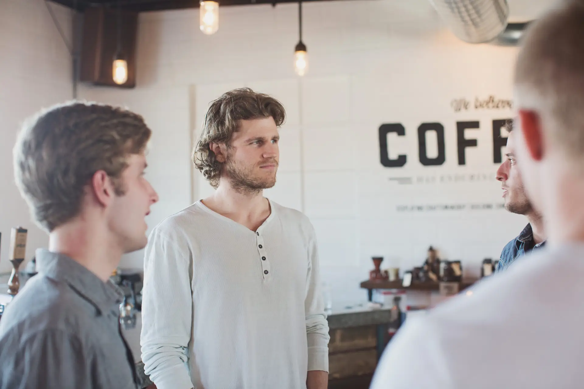 A small group of men stand in a circle talking inside a coffee shop.