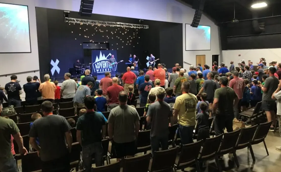 Fathers and sons worship together in large auditorium with band playing on stage