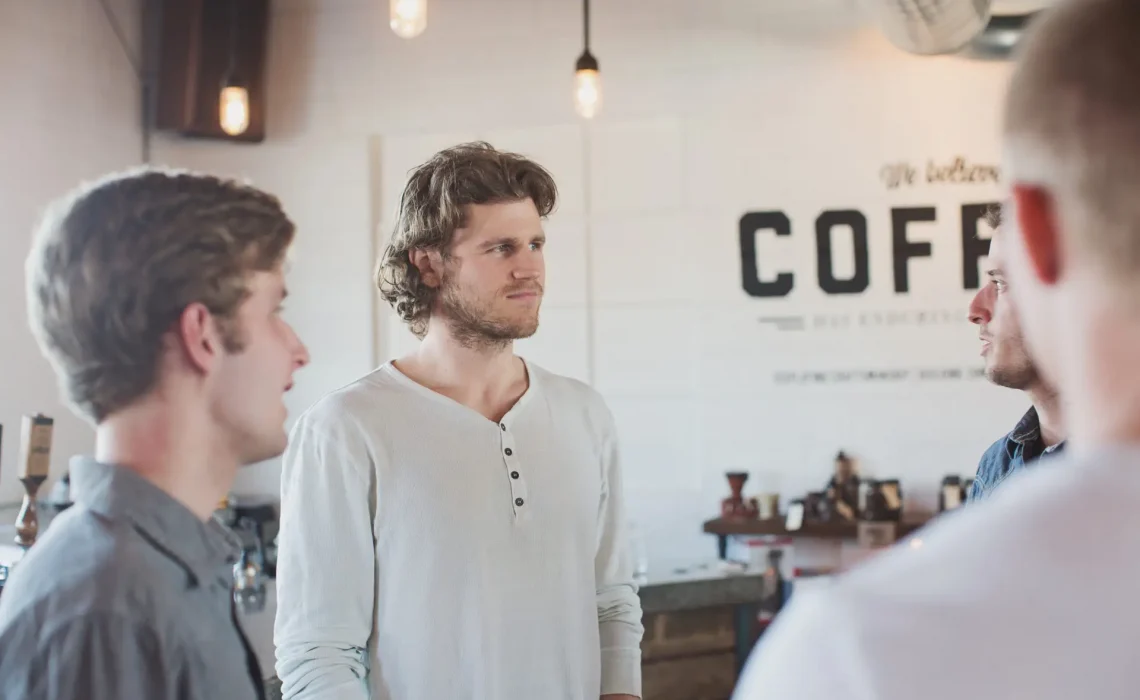 A small group of men stand in a circle talking inside a coffee shop.