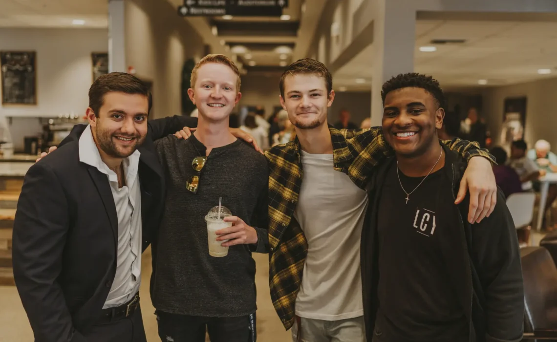 4 guys pose for a picture with arms across each others shoulders