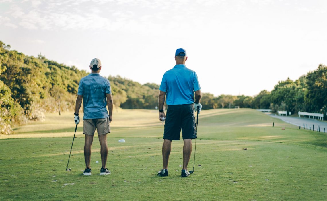 Two men stand facing the fairway on a golf course