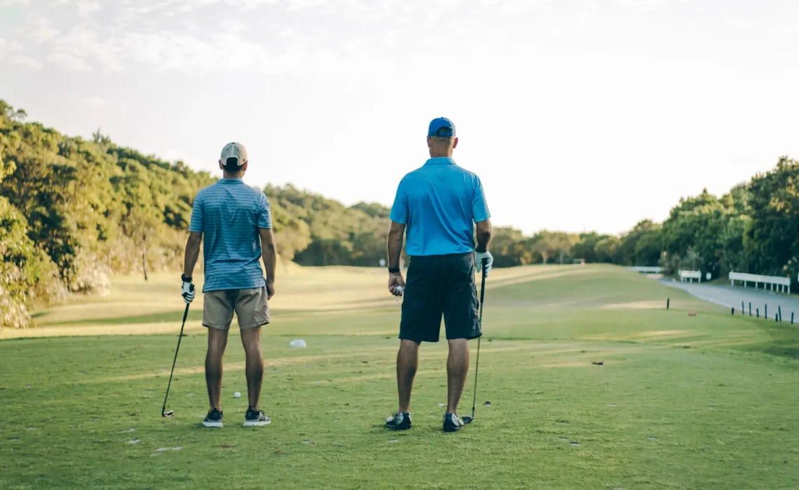 Two men stand facing the fairway on a golf course